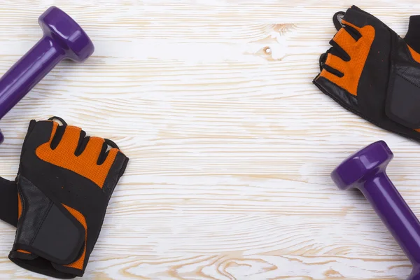 Mancuerna y guantes de fitness sobre fondo de madera — Foto de Stock