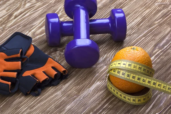 Close-up de halteres, laranja, luvas de fitness e fita métrica — Fotografia de Stock