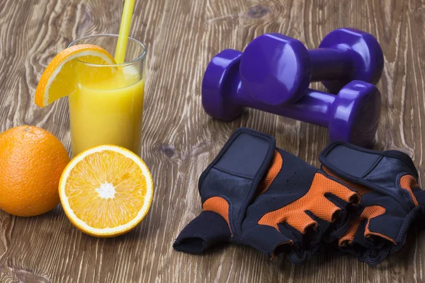 Halteres, suco de laranja, luvas de fitness e fita métrica — Fotografia de Stock