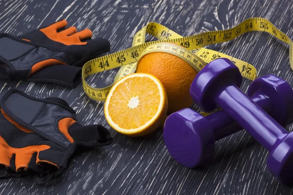 Close-up de halteres, laranja, luvas de fitness e fita métrica — Fotografia de Stock