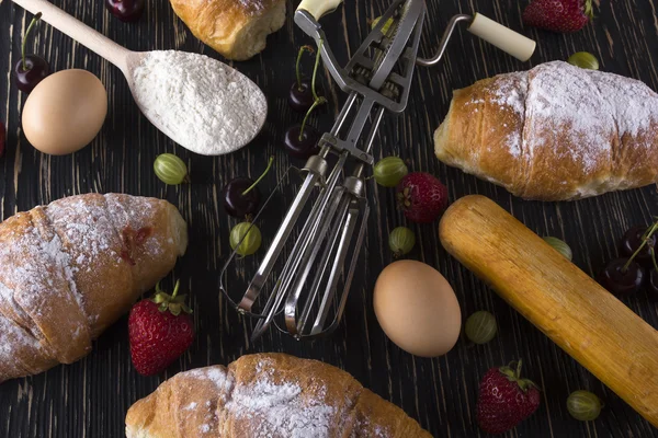 Verse croissants met meel, aardbei, kruisbes, eieren en handvat mixer. — Stockfoto