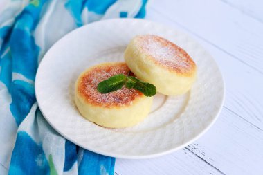 Cheesecake ve nane. Süzme peynirli krep ya da kremalı börek tabağa yakın duran pudra şekerli. Sağlıklı ve diyet kahvaltı.