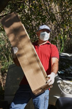 Koruyucu maskeli ve tıbbi eldivenli kurye elinde büyük bir karton teslimat kutusu tutuyor. Ekspres yemek teslimatı ve online alışveriş kavramı. Hızlı teslimat aracı. Karantina.