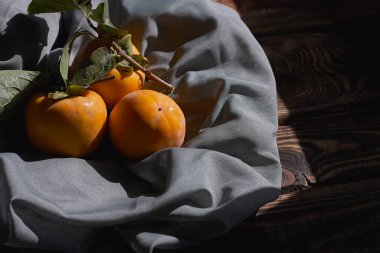 Olgun portakal hurması. Kaki 'yi güneş ışığında koyu mavi kumaşla kaplayın. Sıcak, renkli bir düşüş. Hasat..