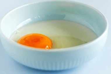 Taze organik yumurta sarısı ve pastel arka planda açık mavi kasede beyaz yumurta. Sağlıklı kahvaltı ve taze malzemeler. Seçici odak.