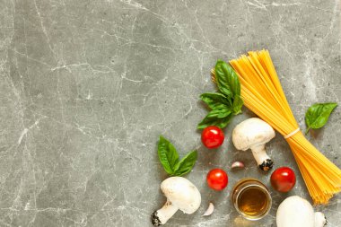 Mantarlı makarna malzemelerinin üst görünümü: spagetti, fesleğen, sarımsak, kiraz ve gri taş zemin üzerinde zeytinyağı