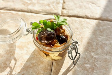 Marinated mushrooms in glass jar, herbs and spices on clear background. Canned vegetatian dish. Natural light. Selective focus. Top view.