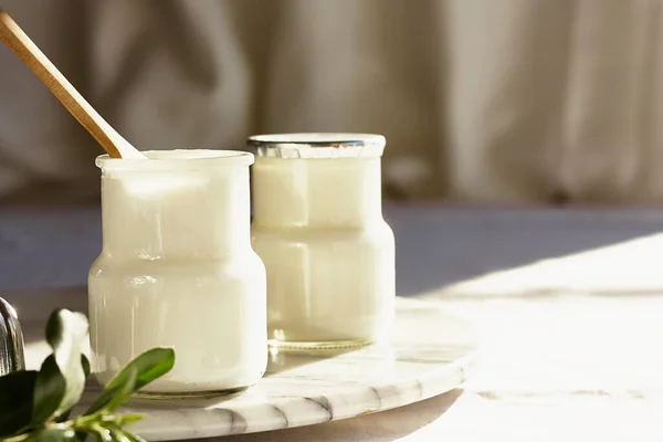 Två portioner av färsk naturlig ekologisk yoghurt i en glasburk på marmorbricka. Hemgjord grekisk yoghurt med träskedar. Sund frukost. — Stockfoto