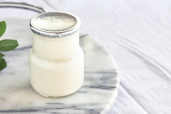 Verse natuurlijke biologische yoghurt in een glazen pot op marmeren dienblad. Zelfgemaakte Griekse yoghurt met houten lepels. Gezond ontbijt. Bovenaanzicht. — Stockfoto