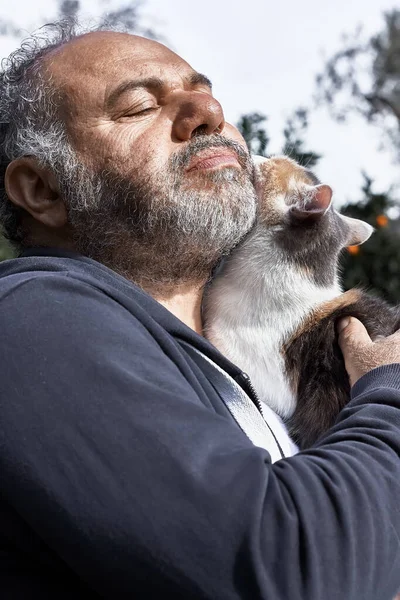 Bearded mature man happy holding and hugging his cute cat. Friendship, love, love of animals, affection concept.