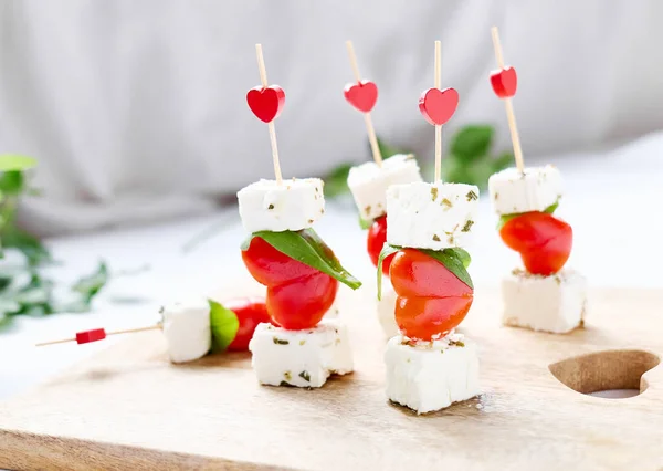 Sevgililer Günü ya da doğum günü romantik atıştırmalıkları. Peynirli ve kalp şeklinde domatesli kanepeler. Sevgililer Günü için orijinal yemek, romantik akşam yemeği. Önplanda seçmeli odak.