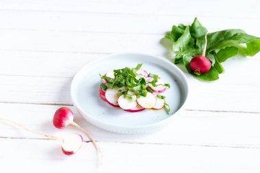 Beyaz ahşap arka planda mavi kasede taze bahar turp salatası. Vejetaryen sebze salatası. Sağlıklı vejetaryen yemeği. Üst görünüm