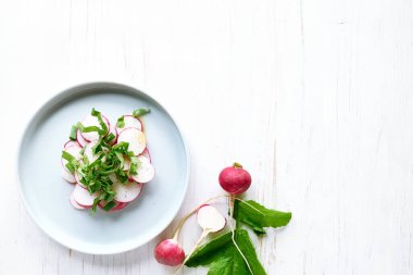 Beyaz ahşap arka planda mavi kasede taze bahar turp salatası. Vejetaryen sebze salatası. Sağlıklı vejetaryen yemeği. Üst görünüm