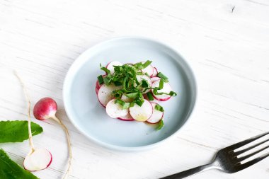 Beyaz ahşap arka planda mavi kasede taze bahar turp salatası. Vejetaryen sebze salatası. Sağlıklı vejetaryen yemeği. Üst görünüm