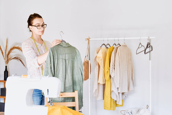 Woman takes linen dress on hanger from clothes rack. Slow Fashion. Conscious consumption. Crisis in the fashion industry, retail. Eco-friendly, Sustainable seasonal Sale concept. Zero waste.
