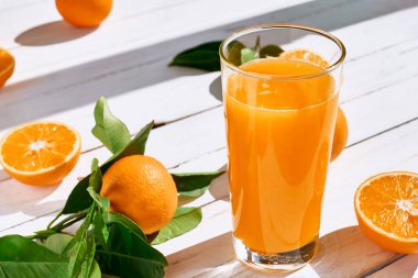 Olgun biyolojik portakallar ve beyaz ahşap arka planda bir bardak taze sıkılmış portakal suyu. Organik Sicilya portakalları