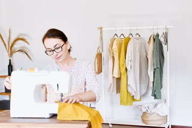 Küçük bir stüdyoda dikiş makinesine dikiş diken bir kadın. Moda atölyesi, terzilik, el yapımı kıyafetler, endüstri, konsept. Yavaş moda. Bilinçli tüketim.