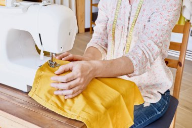 Küçük bir stüdyoda dikiş makinesine dikiş diken bir kadın. Moda atölyesi, terzilik, el yapımı kıyafetler, endüstri, konsept. Yavaş moda. Bilinçli tüketim.
