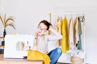 Terzi, küçük moda stüdyosundaki dikiş makinesinin önünde grafik tabletinde bir çizim yapıyor. Moda atölyesi, terzilik, el yapımı kıyafetler, endüstri, konsept. Yavaş Moda.