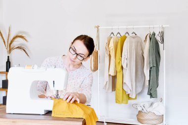 Küçük bir stüdyoda dikiş makinesine dikiş diken bir kadın. Moda atölyesi, terzilik, el yapımı kıyafetler, endüstri, konsept. Yavaş moda. Bilinçli tüketim.