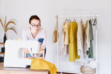 Küçük moda stüdyosundaki dikiş makinesinin önünde terzi sohbeti. Moda atölyesi, terzilik, el yapımı kıyafetler, endüstri, konsept. Yavaş Moda.