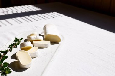 Lezzetli peynir peyniri ya da seramik kesim tahtasının üzerinde beyaz masa örtülü otlar olan camembert peyniri. Süt ürünleri. İtalyan, Fransız peyniri. Kahvaltı..