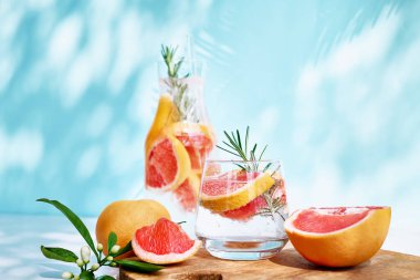 Greyfurtlu, biberiyeli ve sulu narenciye dilimli yaz kokteyli. Gölgeli, güneş ışığında taze, sağlıklı greyfurt içeceği. Mavi pastel arka planda yaratıcı içecek.