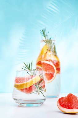 Greyfurtlu, biberiyeli ve sulu narenciye dilimli yaz kokteyli. Gölgeli, güneş ışığında taze, sağlıklı greyfurt içeceği. Mavi pastel arka planda yaratıcı içecek.
