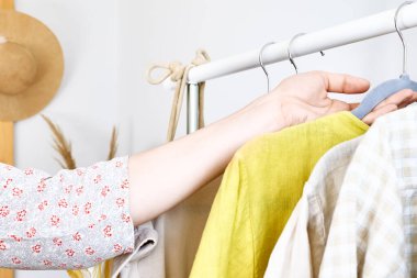 Kadın elbise askılığından keten elbise alıyor. Slow Fashion. Bilinçli tüketim. Moda endüstrisinde kriz, perakende. Çevre dostu, sürdürülebilir mevsimsel satış konsepti. Sıfır atık.