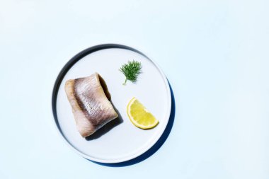 Limon dilimi ve açık mavi arka planda dereotlu ringa filetosu. Minimum gıda konsepti. Klasik marine edilmiş ringa dürümleri..