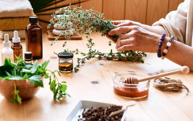 Kadın, masadaki aromaterapi seansını temel yağ dağıtıcı tıbbi bitkilerle, farklı yağ ve esanslarla hazırlıyor. Aromaterapi ve alternatif tıp konsepti. Doğal ilaçlar..