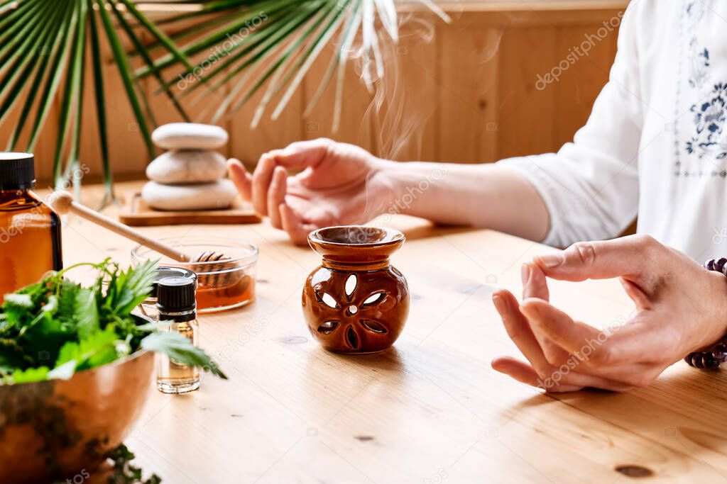 Woman has aromatherapy session at the table with essential oil diffuser medical herbs, different types of oils and essences. Aromatherapy and alternative medicine concept. Natural remedies.