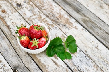 Bahçedeki ahşap masada bir kasede taze, olgun organik biyo çilekler. Bahar ya da yaz hasadı. Sağlıklı beslenme. Vitamin.