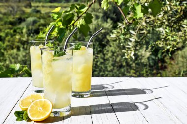 Bahçedeki beyaz ahşap masada limonatalı bardakları iç. Limon detoks içeceği, yaz aylarında alkolsüz kokteyl. Sağlıklı konsept