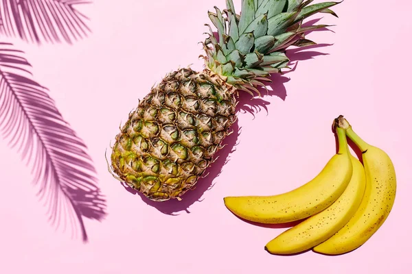 Summer creative tropic fuit layout. Pineapple and banana on pink pastel background with palm leaf. Healthy food summertime concept. Top view. Copy space.