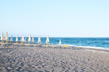 Terkedilmiş çakıl taşı plajı, güverte sandalyeleri ve akşamları kapalı şemsiyeler. Sicilya turistik bir yer. Akdeniz 'de mevsim. İyon Denizi