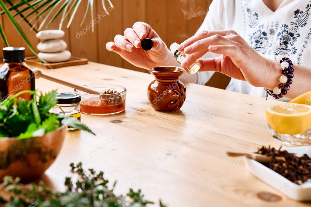 Woman prepares aromatherapy session at the table with essential oil diffuser medical herbs, different types of oils and essences. Aromatherapy and alternative medicine concept. Natural remedies.
