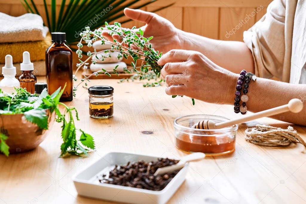 Woman prepares aromatherapy session at the table with essential oil diffuser medical herbs, different types of oils and essences. Aromatherapy and alternative medicine concept. Natural remedies.