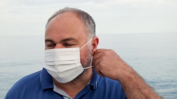 Чоловік знімає захисну маску зі свого обличчя і глибоко дихає на пляжі біля моря в літній день після закінчення епідемії коронавірусу . — стокове відео