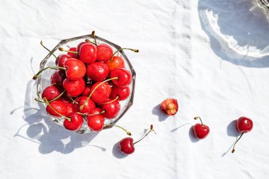 Masadaki cam kasede beyaz masa örtüsüyle taze, olgun kirazlar. Yaz mevsimi tatlı organik meyveler. Üst Manzara. Seçici odak.