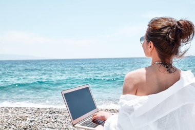 Kumsalda dizüstü bilgisayar kullanan başarılı bir kadın. Açık havada çalışan bir iş kadını. Teknoloji ve seyahat, serbest konsept. Modern ofis. Uzak çalışma.