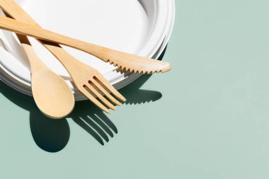 Çevre dostu bambu çatal bıçak seti ve açık yeşil pastel arka planda biyolojik çözünebilir plakalar. Sıfır atık, plastiksiz yaşam tarzı konsepti.