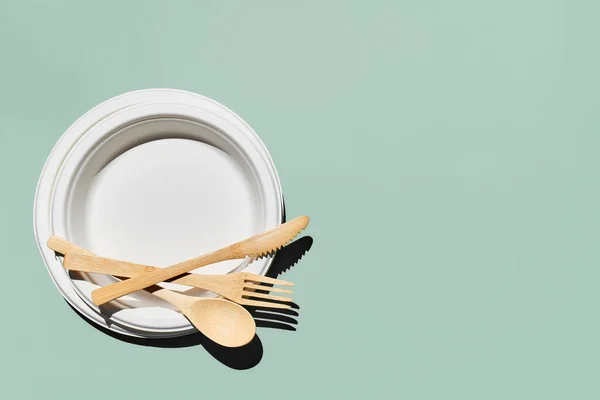 Çevre dostu bambu çatal bıçak seti ve açık yeşil pastel arka planda biyolojik çözünebilir plakalar. Sıfır atık, plastiksiz yaşam tarzı konsepti.