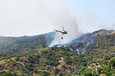 Yangın helikopteri dağlardaki bir orman yangınında kovadan su bırakıyor. Orman yangını çevresel bir felakettir. Ormanların tahrip edilmesi.