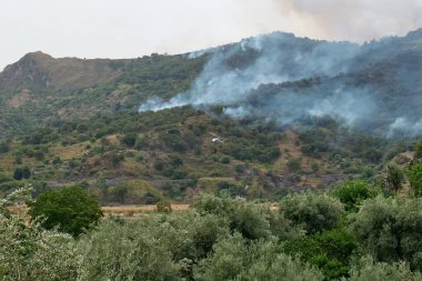 Yangın helikopteri dağlardaki bir orman yangınında kovadan su bırakıyor. Orman yangını çevresel bir felakettir. Ormanların tahrip edilmesi.