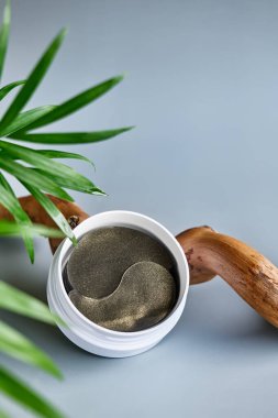 Üzerinde hidrojel göz bantları olan beyaz krem kavanozu, pastel gri arka planda, ahşap kapağın yanında. Ürün sunumu. Eko-biyoloji kozmetik konsepti. Kozmetik veya güzellik ürünü tanıtım modası minimalist modelleme.