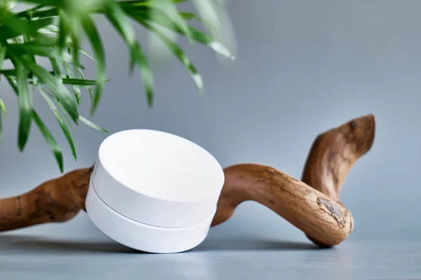 Pastel gri arka planda ahşap kapaklı beyaz krema kavanozu. Kozmetik ürün reklamcılığı için sunum aşaması. Eko-biyoloji kozmetik konsepti. Güzellik ürünü tanıtım modası Minimalist modelleme.