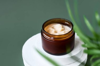 Beyaz alçı taşı silindir podyumunda açık kahverengi krema kavanozu ve ürün sunumu için pastel yeşil arka planda palmiye yaprakları. Soyut kaide. Kozmetik ya da güzellik ürünü tanıtım modası minimalist modelleme