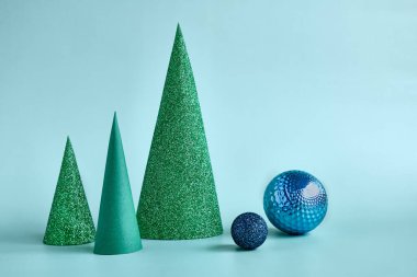 Güzellik ürünleri için soyut noel kompozisyonları. Geometrik Kağıt Noel ağaçları, beyaz alçıtaşı kaidesinin yanında ve turkuaz pastel arka planda mavi noel topları. Kış indirimi.