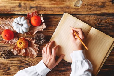 Sonbahar yatağı. Bir kadının elleri, açık bir kitabın üzerine, bir balkabağının yanında, renkli bir sonbahar meyvesi ve ahşap masa manzarasında kurumuş yapraklarla yazar. Samimi düşüş havası. kopyalama alanı. Şükran Günü.